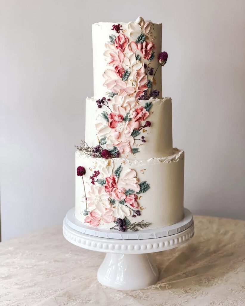 three tier ivory white buttercream cake with palette flowers in pinks and burgundy